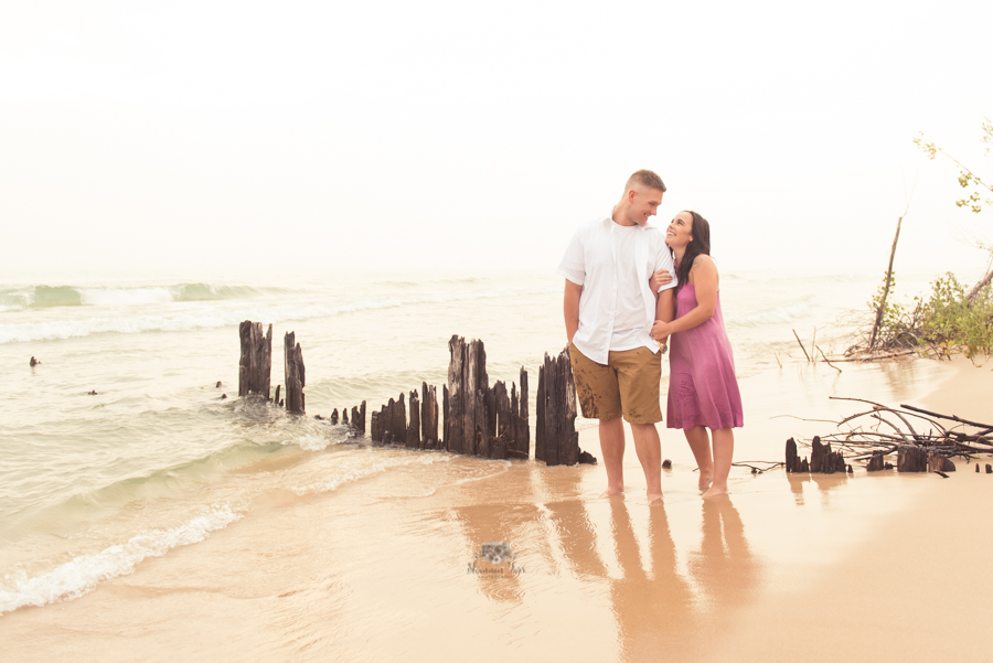 Engagement Photography in Ludington MI of couple standing on beach looking at each other