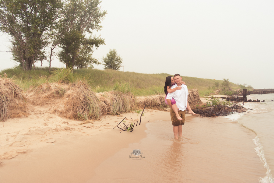 Engagement Photography in Ludington MI of couple standing on beach giving a piggy back ride