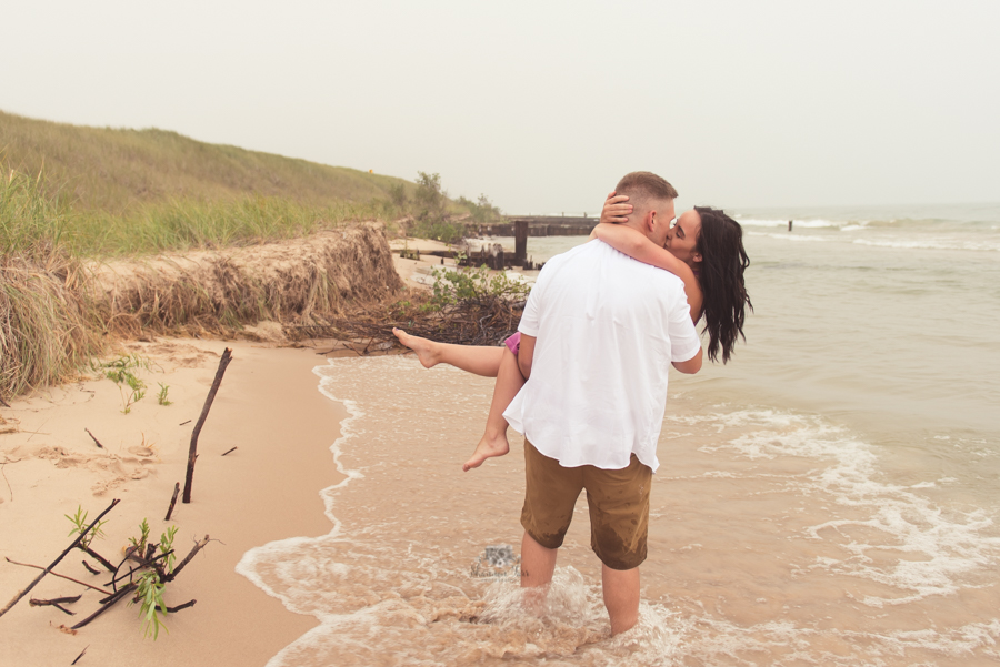 Engagement Photography in Ludington MI of guy standing on beach kissing his bride to be