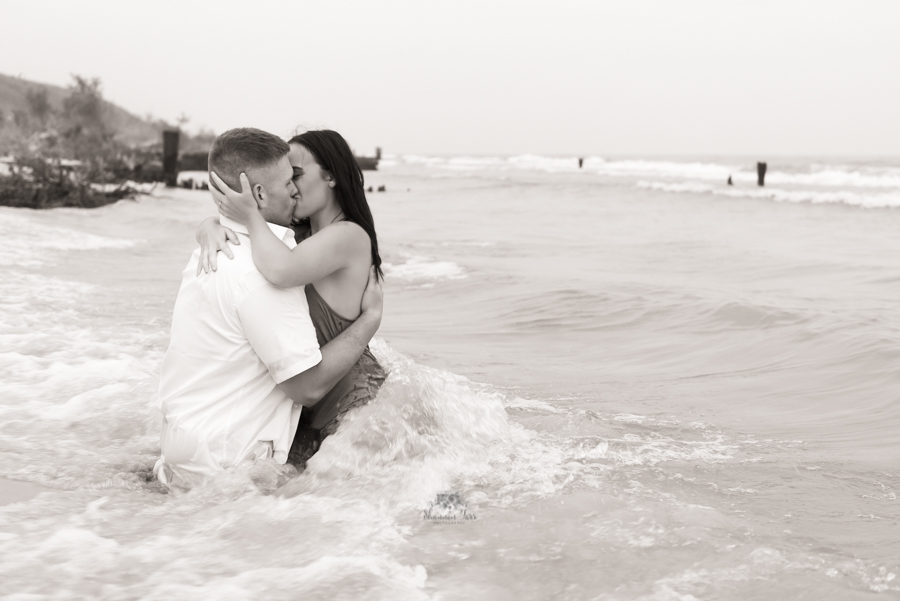 Engagement Photography in Ludington MI of couple sitting in water passionately kissing 